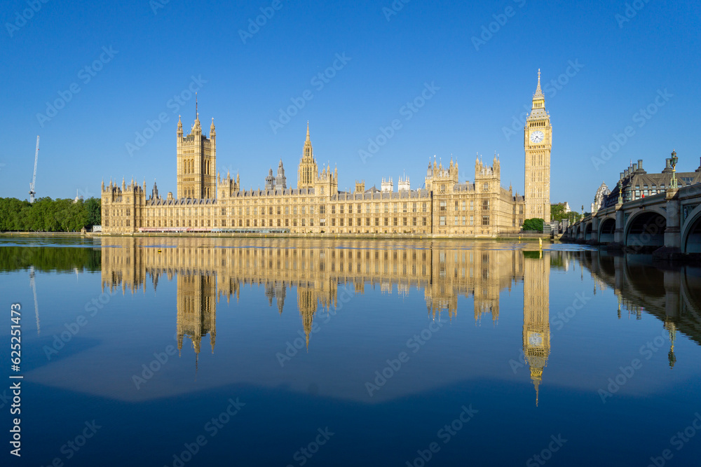 Photo of the London Parliament with the tower of Big Ben, reflected in the water of the River Thames. On a sunny morning.