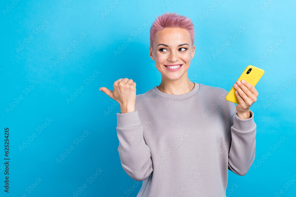 Photo of attractive positive lady beaming smile hold smart phone look indicate finger empty space isolated on blue color background
