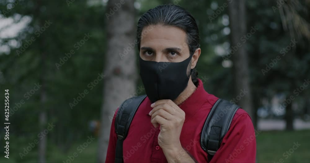 Slow motion portrait of Arab man with backpack putting on medical face mask standing in city outdoors. Healthcare and pandemic concept. Slow motion portrait of Arab man with backpack putting on medical face mask standing in city outdoors. Healthcare and pandemic concept.
