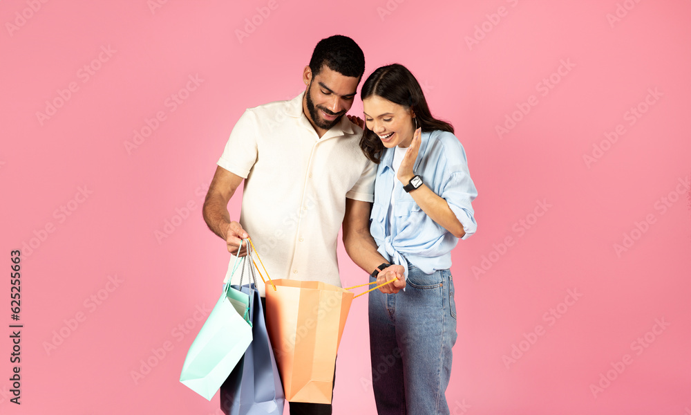 Happy young woman looking inside paper bag, shopping with boyfriend Happy young woman looking inside paper bag, shopping with boyfriend