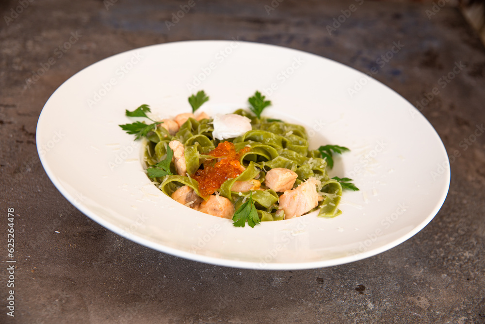 green pasta with salmon and red caviar and greens in a white plate green pasta with salmon and red caviar and greens in a white plate