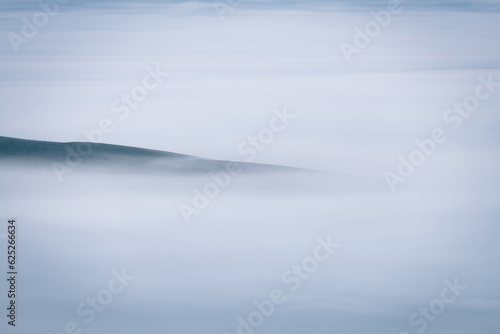 Mountains in a fog illuminated by rising sun. Autumn landscape with vivid sunlight.