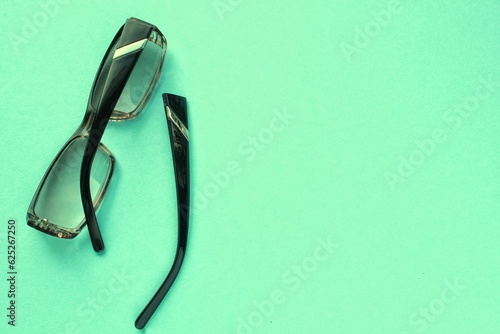 Old broken eyeglasses with damaged legs on green background. Poor eyesight. Reuse and repair concept. Idea of health. Failure optic eyewear. Breakage of vision correction glasses. Close up, flat lay