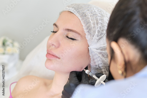 cosmetology clinic, where skilled aesthetician is seen injecting filler into jowls. procedure, focusing on reducing masseter lines and enhancing face shape photo