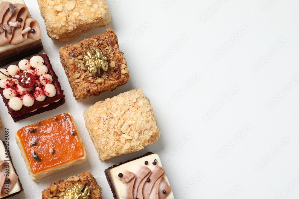 Pieces of different delicious cakes on white table, flat lay. Space for text Pieces of different delicious cakes on white table, flat lay. Space for text