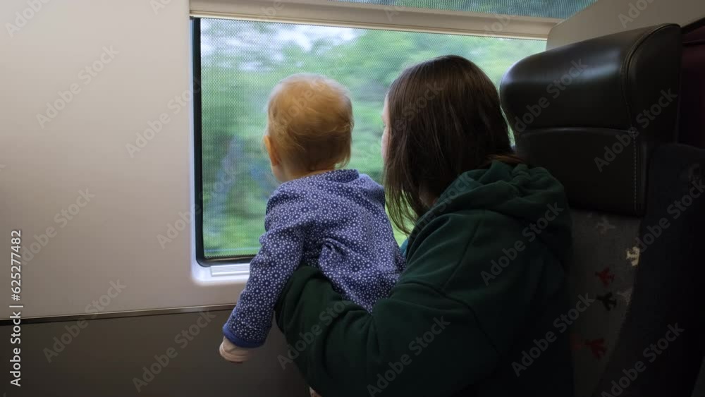 Young woman with her cute baby enjoying train journey, mother with infant daughter looking out the window Young woman with her cute baby enjoying train journey, mother with infant daughter looking out the window