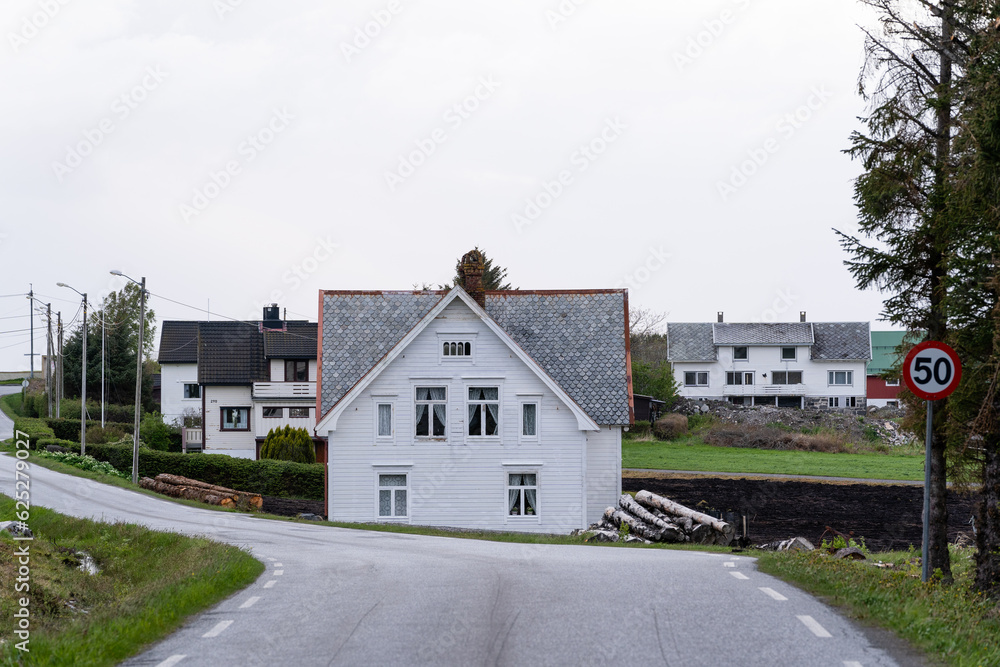 Asphalted light gray road with a white wooden house in front with a gray stone roof above a light bright sky Asphalted light gray road with a white wooden house in front with a gray stone roof above a light bright sky