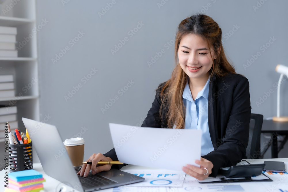Happy Asian woman accountant at work sitting and taking note of the office report. Asian businesswoman writing a note making a report on investment profits earnings of a company. Happy Asian woman accountant at work sitting and taking note of the office report. Asian businesswoman writing a note making a report on investment profits earnings of a company.