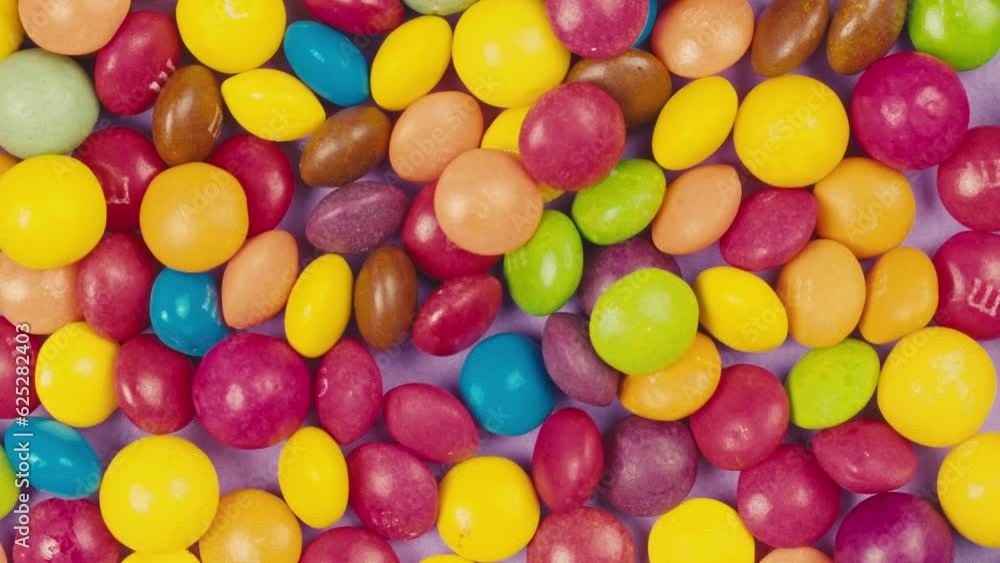 Colorful dragee candies lollipops with glitter sprinkles on purple background. Summer bright texture studio shot for store, supermarket, close-up top view, zoom. Children sweets made of sugar. Colorful dragee candies lollipops with glitter sprinkles on purple background. Summer bright texture studio shot for store, supermarket, close-up top view, zoom. Children sweets made of sugar.