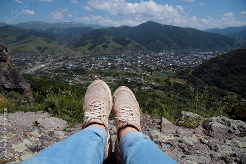 Women's legs in light sneakers, view from a high mountain, active hiking