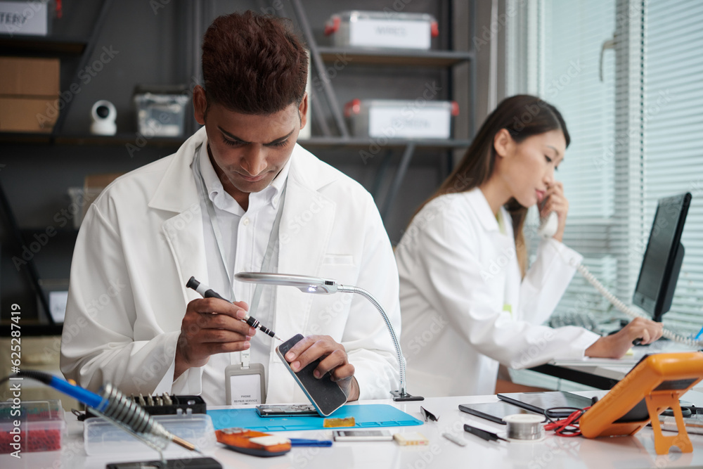 Technician reassembling smartphone when manager talking on phone with client Technician reassembling smartphone when manager talking on phone with client
