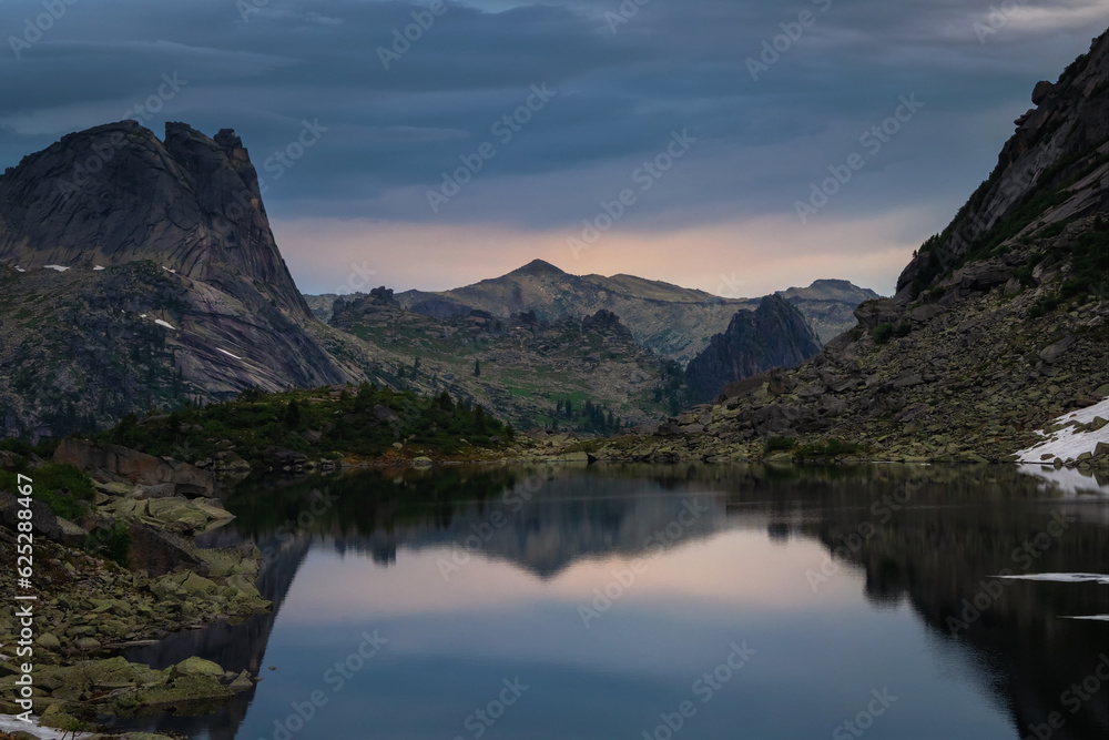 Stunning dawn on the lake. Mountain Spirits Lake in Ergaki on an summer morning among the taiga rocks with dramatic sky and tree Mountain landscape. Ergaki Nature Park in the mountains of Siberia.