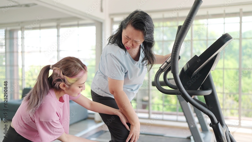 Obraz premium Asian elderly women suffering pain from exercising on the machine and young daughter rushed to take care. Young women take care knee pain of her mother while exercising. Pain from exercise