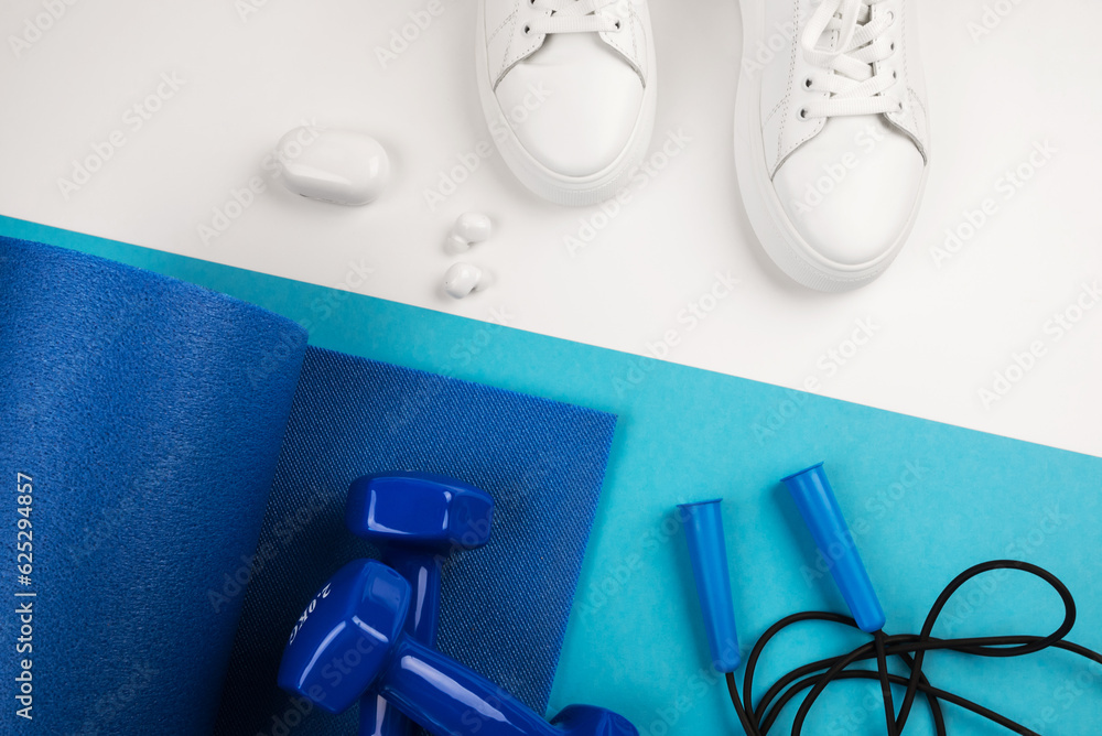 Top view photo of blue dumbbells, blue exercise mat and other sports equipment on blue and white background. Top view photo of blue dumbbells, blue exercise mat and other sports equipment on blue and white background.