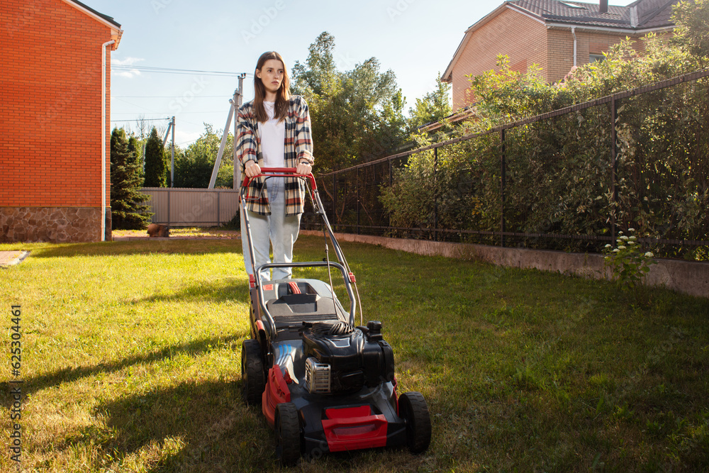 Female gardener working in summer, cutting grass in backyard. Concept of gardening, work, nature. Housework, gardening and country life. Home garden grass cutting woman mowing with lawn mower. Female gardener working in summer, cutting grass in backyard. Concept of gardening, work, nature. Housework, gardening and country life. Home garden grass cutting woman mowing with lawn mower.
