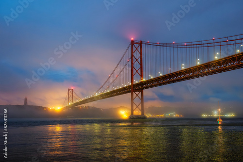 View of 25 de Abril Bridge famous tourist landmark of Lisbon connecting Lisboa and Almada in heavy fog mist wtih yacht boats passing under. Lisbon, Portugal © Dmitry Rukhlenko