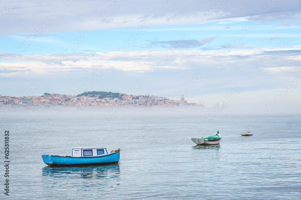 Fishing boats in Tagus river on misty morning with Lisbon in background with mist. Lisbon, Portugal