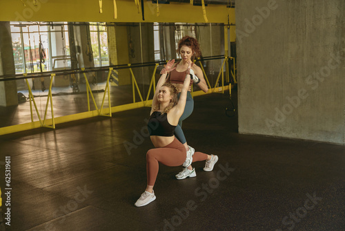 Fit young woman doing stretching exercises with the help of personal trainer at gym