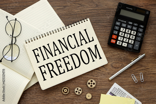 glasses and a calculator lie on a notebook with words Financial freedom