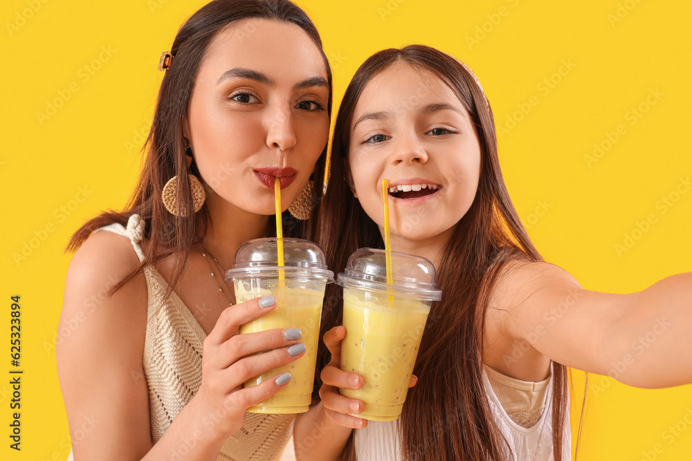 Little girl with her mother drinking smoothie on yellow background, closeup Little girl with her mother drinking smoothie on yellow background, closeup