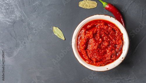 Hot pepper paste and harissa sauce. Adjika on a black background. Traditional Tunisian, Georgian and Arabic cuisine. Homemade harissa rose in a bowl. Copy space flat lay, top view.