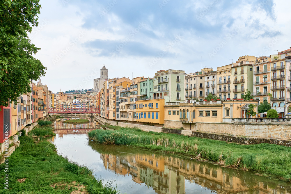 Colorful yellow and orange houses and bridge Pont de Sant Agusti reflected in water river Onyar, in Girona, Catalonia, Spain. Church of Sant Feliu and Saint Mary Cathedral at background. BRIDGE in the