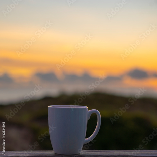 A white coffee cup with a sunset behind it 