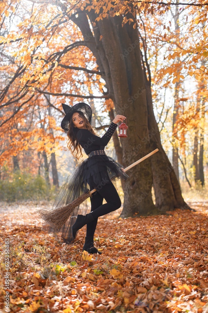 Woman in witch costume standing in autumn forest on Halloween