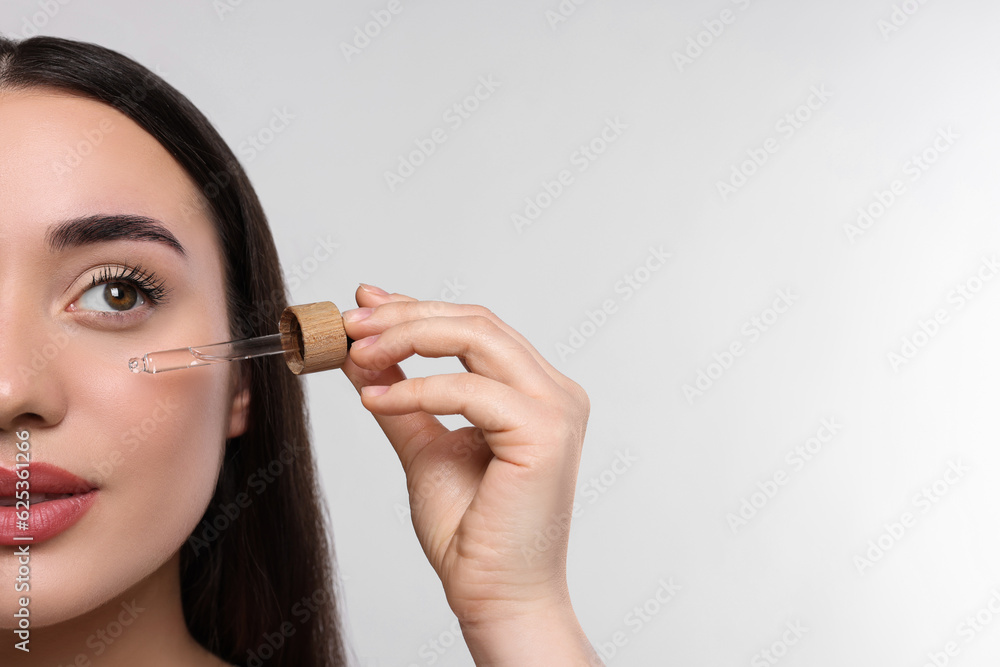 Young woman applying essential oil onto face on white background, closeup and space for text