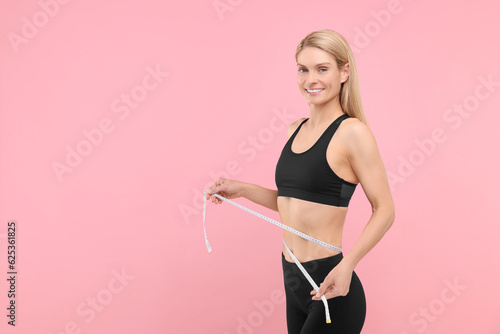 Slim woman measuring waist with tape on pink background, space for text. Weight loss © New Africa