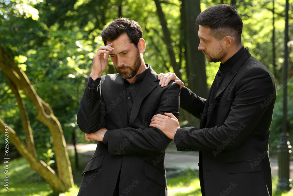 Funeral ceremony. Man comforting his friend outdoors Funeral ceremony. Man comforting his friend outdoors