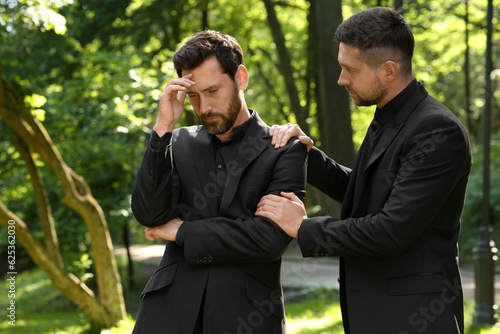 Funeral ceremony. Man comforting his friend outdoors