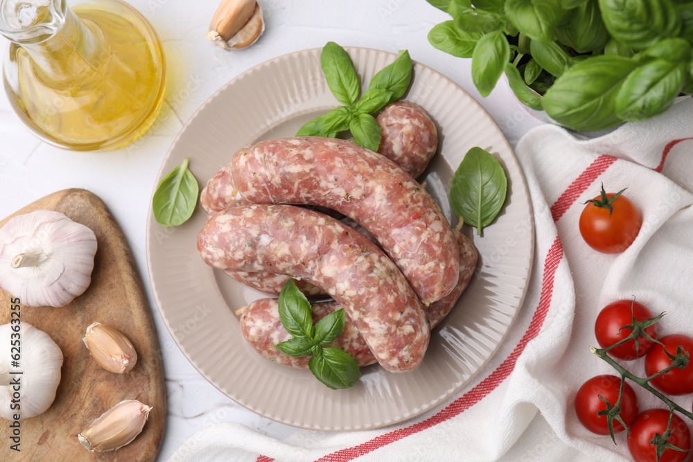 Raw homemade sausages and different products on white table, flat lay