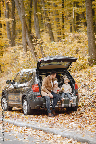 Father and his children sitting at open trunk of hatchback car in autumn forest