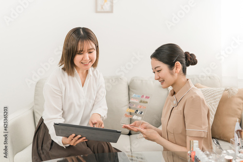 ネイルサロンでプランとデザインを説明するネイリストと見本を見ながらタブレットで選ぶ日本人女性 