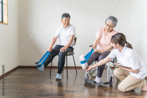 介護施設でチューブトレーニング・リハビリする車椅子のシニア・高齢者と理学療法士・介護士・トレーナー 