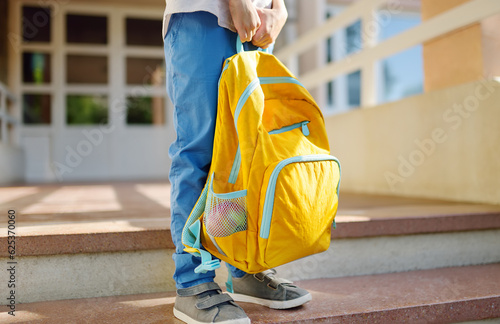 Little student with a backpack on the steps of the stairs of school building. Close-up of child legs, hands and schoolbag of boy standing on staircase of schoolhouse.Back to school concept.