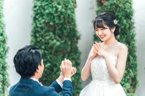 プロポーズで指輪・エンゲージリングをプレゼントされるウェディングドレスを着た笑顔のアジア人女性・新婦 