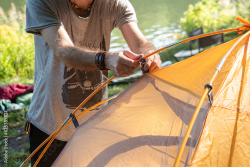 Young man preparing camping tent against river