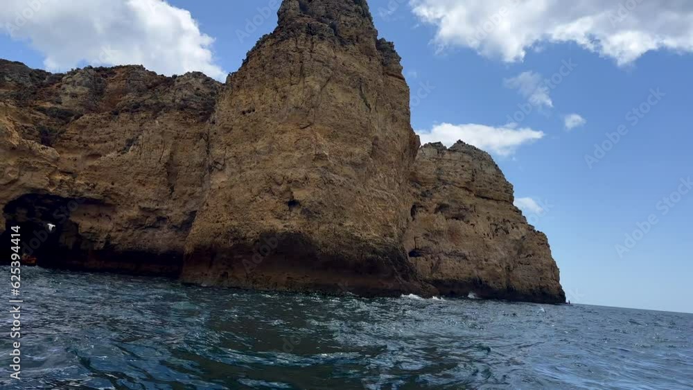 Wide shot of gigantic rocky cliff coastline at Algarve with wavy ocean water - pov shot from boat Wide shot of gigantic rocky cliff coastline at Algarve with wavy ocean water - pov shot from boat