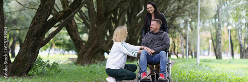 Happy disabled person in wheelchair and two women take care of him in park.