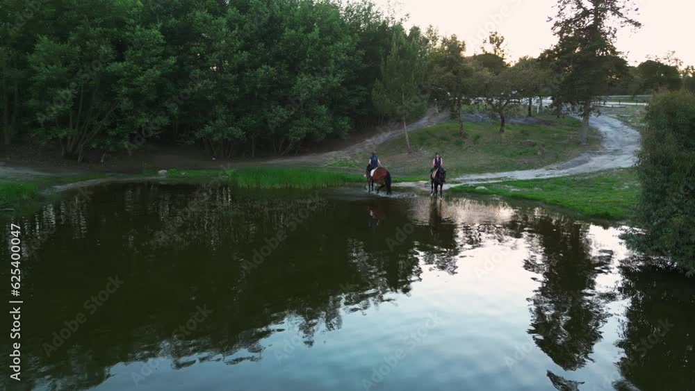 Drone shot of women riding horses through pond water, sunny evening in Portugal Drone shot of women riding horses through pond water, sunny evening in Portugal