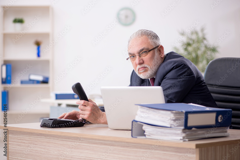 Old male employee talking by phone in the office Old male employee talking by phone in the office