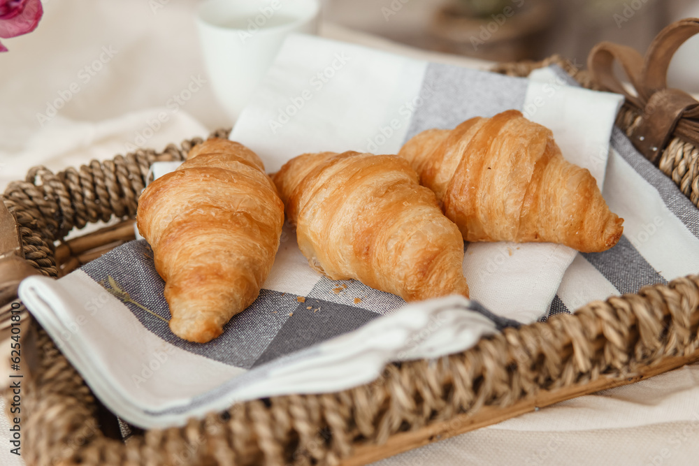 Fresh croissants in a wicker basket on the table next to a vase of lilac tulips.