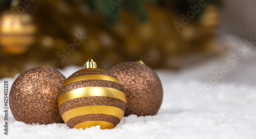 Three Christmas golden balls lie on a white plaid against the background of a Christmas tree and a glowing garland photo