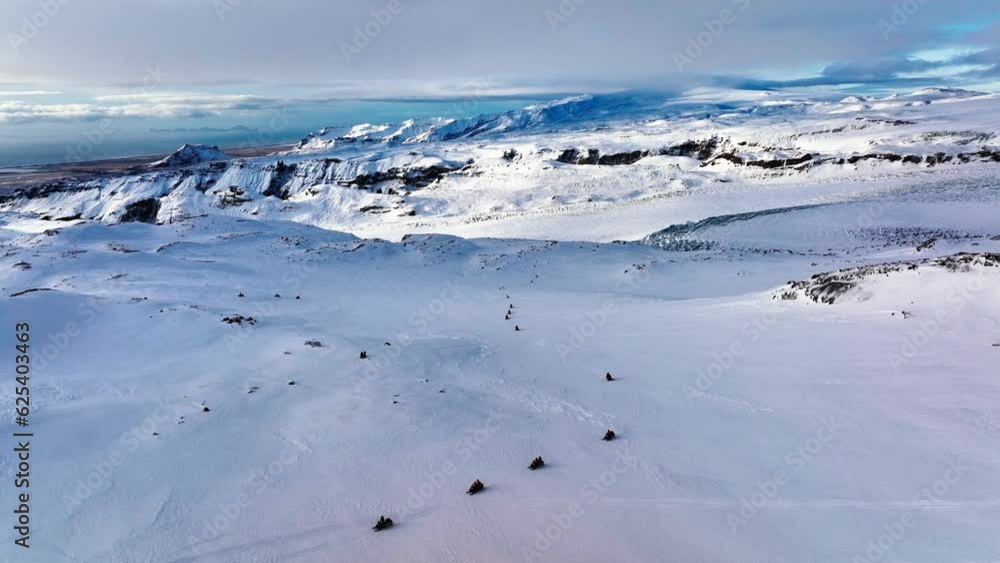 Aerial panoramic landscape view of people riding snowmobiles on the frozen ground of Myrdalsjokull glacier in Iceland, at dusk Aerial panoramic landscape view of people riding snowmobiles on the frozen ground of Myrdalsjokull glacier in Iceland, at dusk