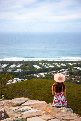 beautiful woman in colorful dress and elegant hat watching panorama of coolum beach and sunshine coast from the top of mount coolum  queensland  australia 