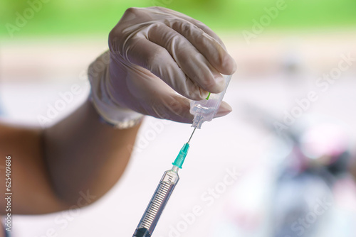 Doctor hands holding a vaccine bottle and syringe with needle filling with transparent fluid.