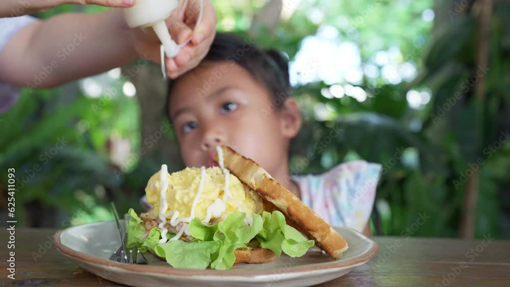 Mother pouring mayonnaise and tomato ketchup on scrambled eggs tuna sandwiches for her child.