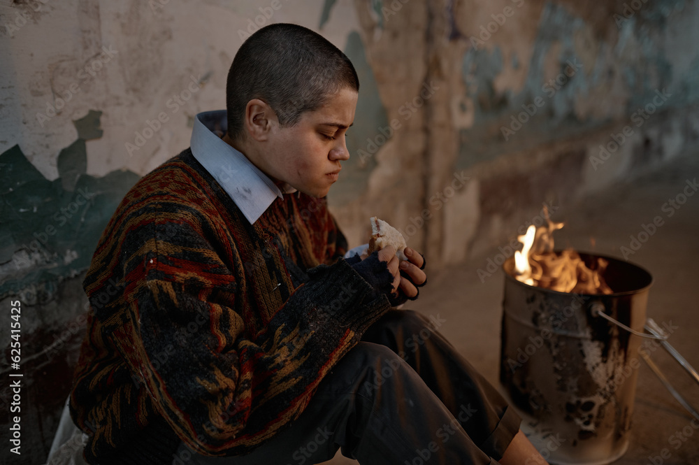 Obraz premium Poor homeless woman eating sandwich while warming at bonfire
